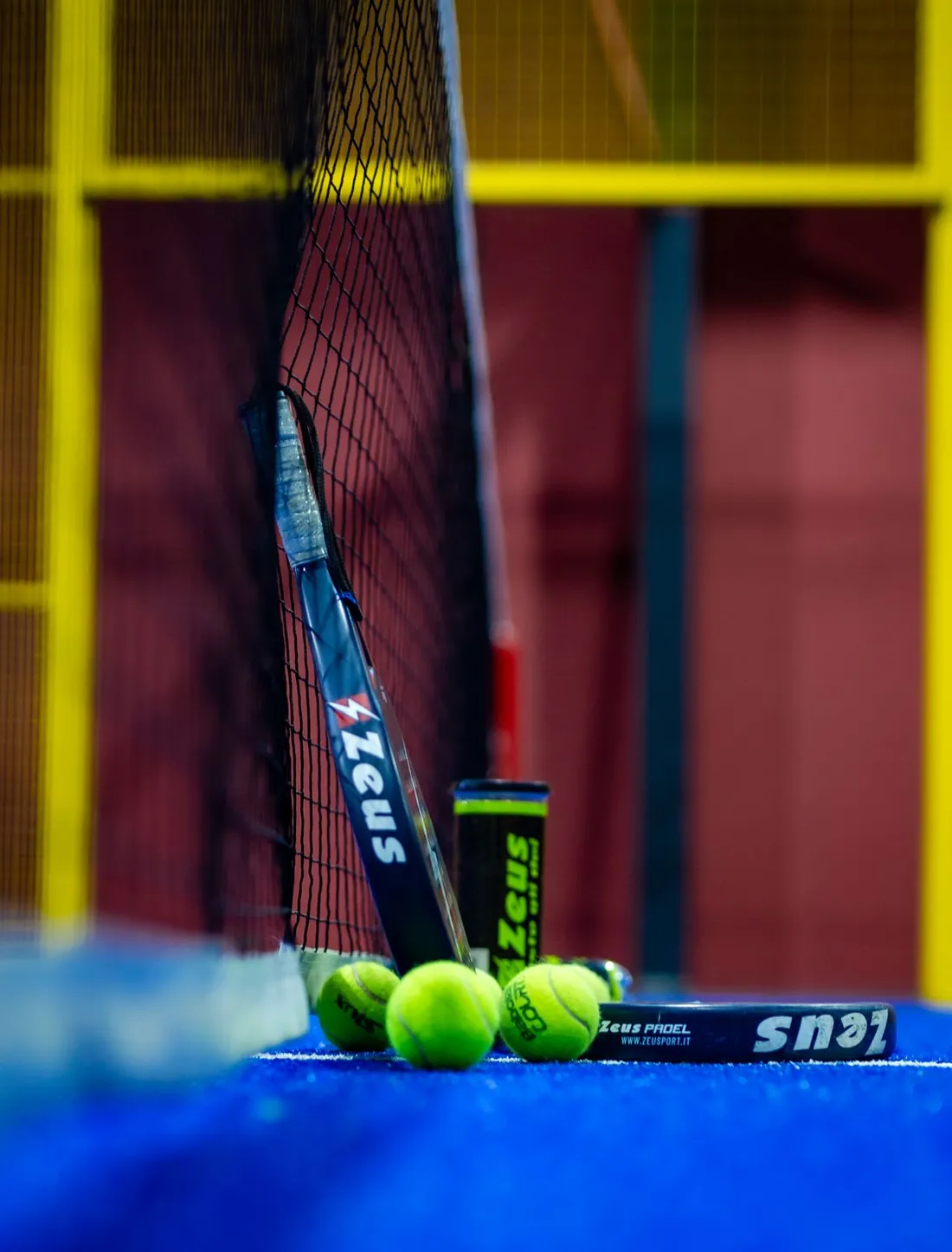 Raquette de padel, balles et tube posés contre le filet d'un terrain