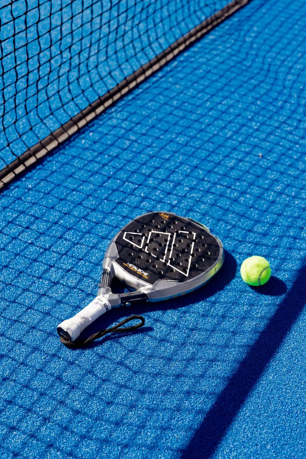 Raquette de padel et balle posées sur un terrain bleu près du filet