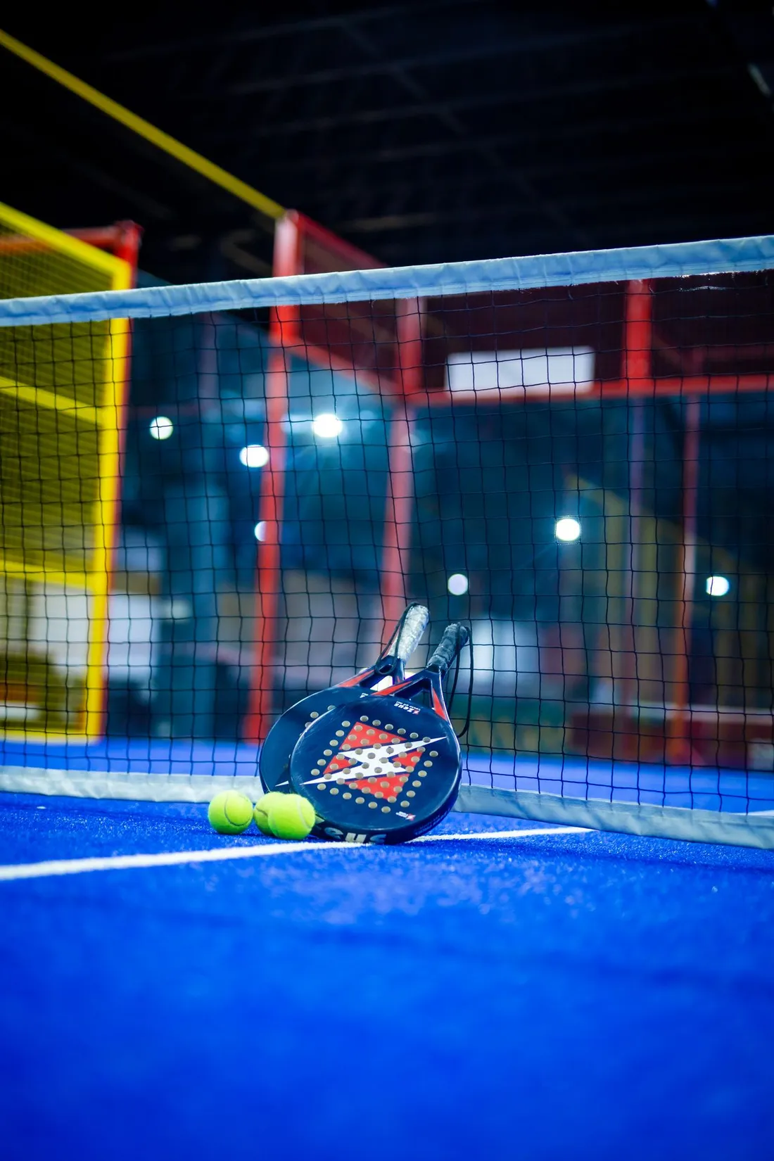 Terrain de padel indoor avec raquette et balles au pied du filet